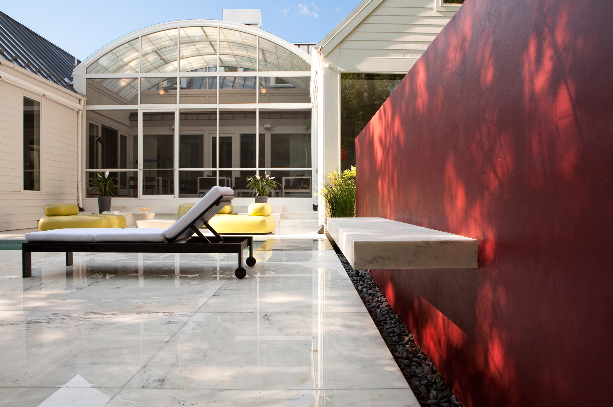 White marbled tile on an outdoor patio with a red accent wall holding a slab of granite as a table