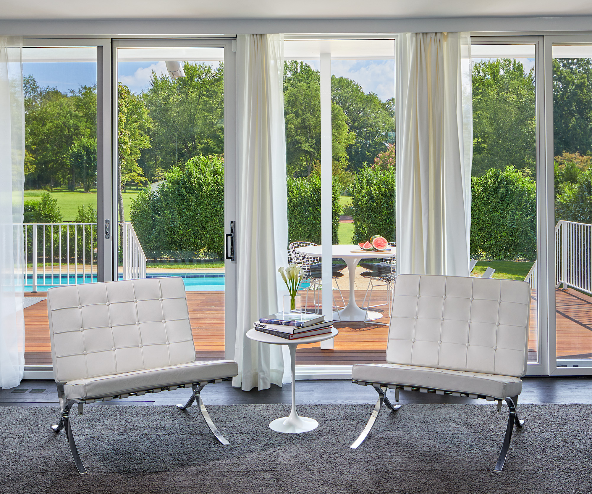 Modern silver and white accent chairs in a living room overlooking the backyard deck and pool