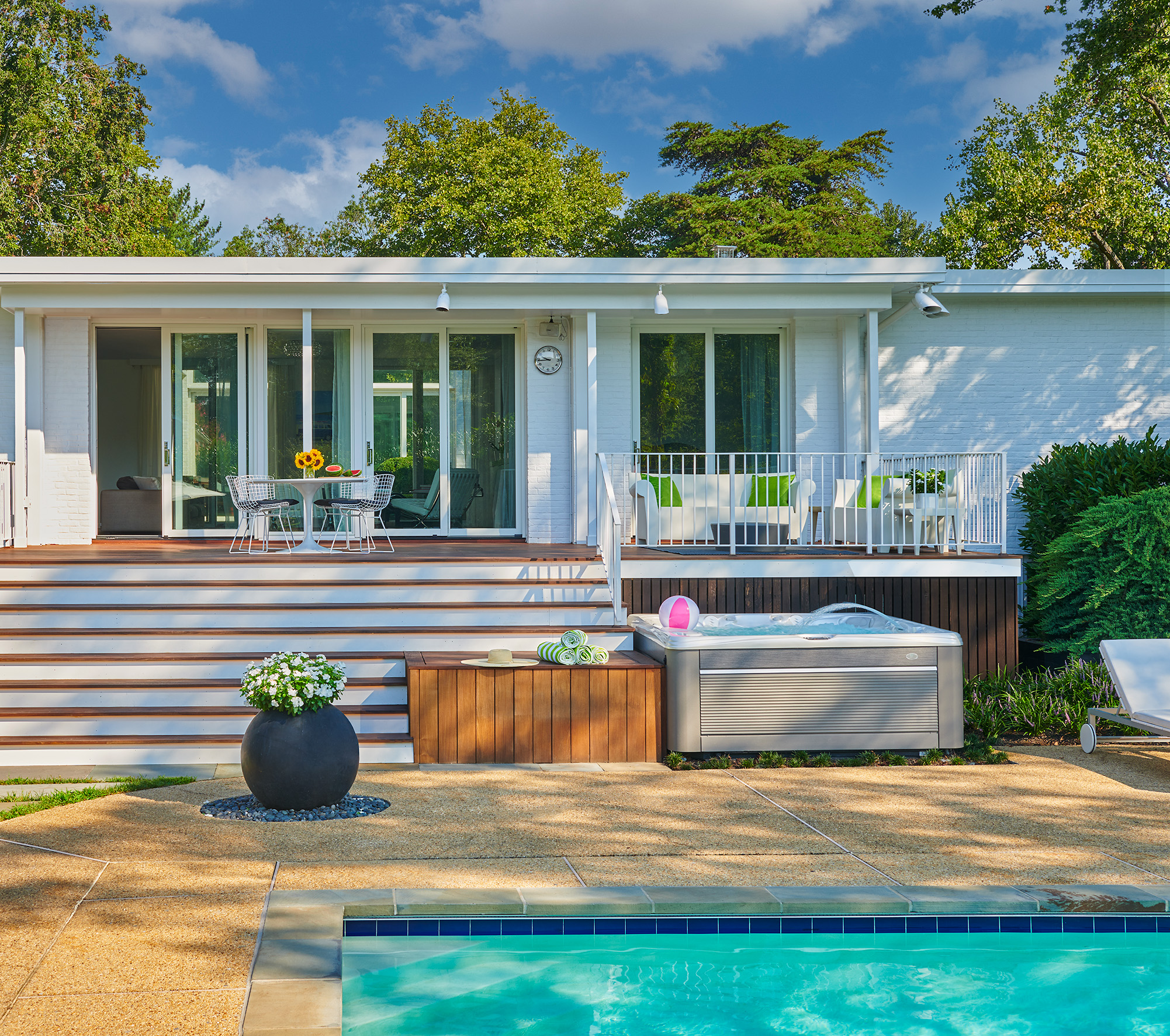Back of house view of a modern white brick home. Pool and hot tub below the wood decking