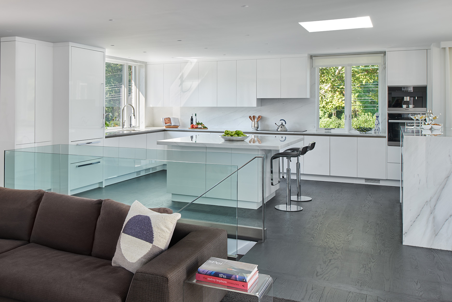 Glass bordered staircase leading up to a modern white kitchen with dark hardwood floors