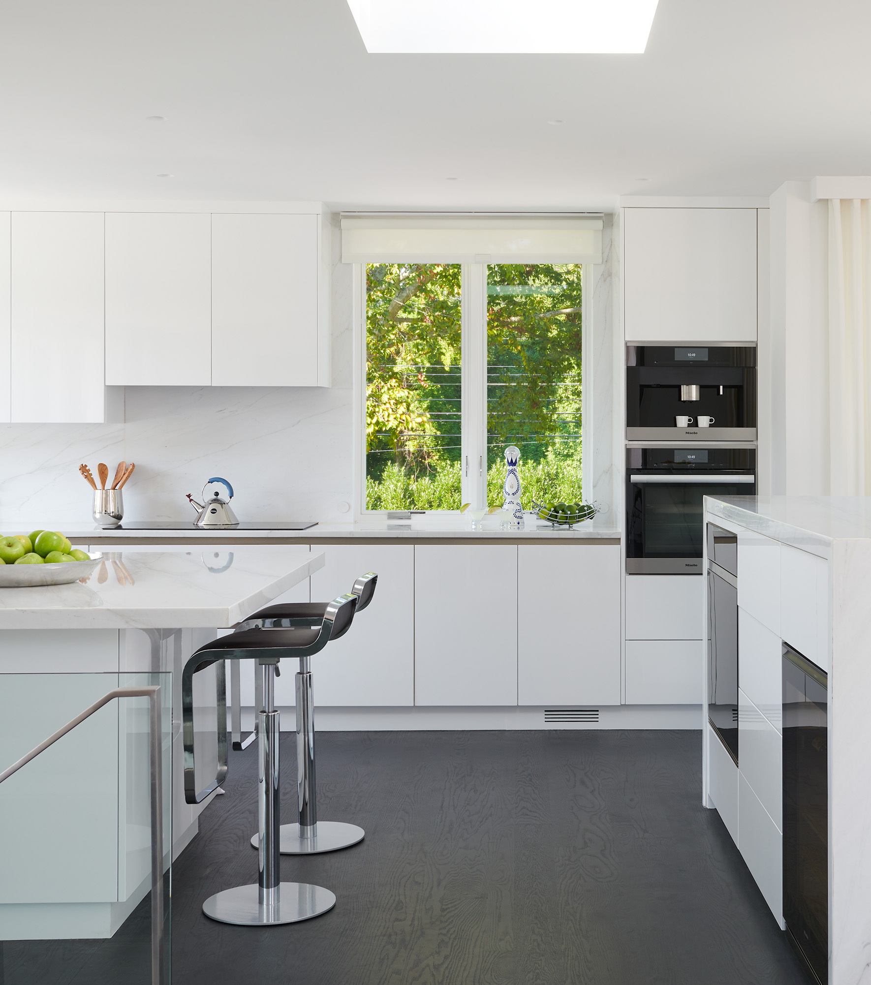 High-top barstools at a marbled granite island countertop in a white modern kitchen