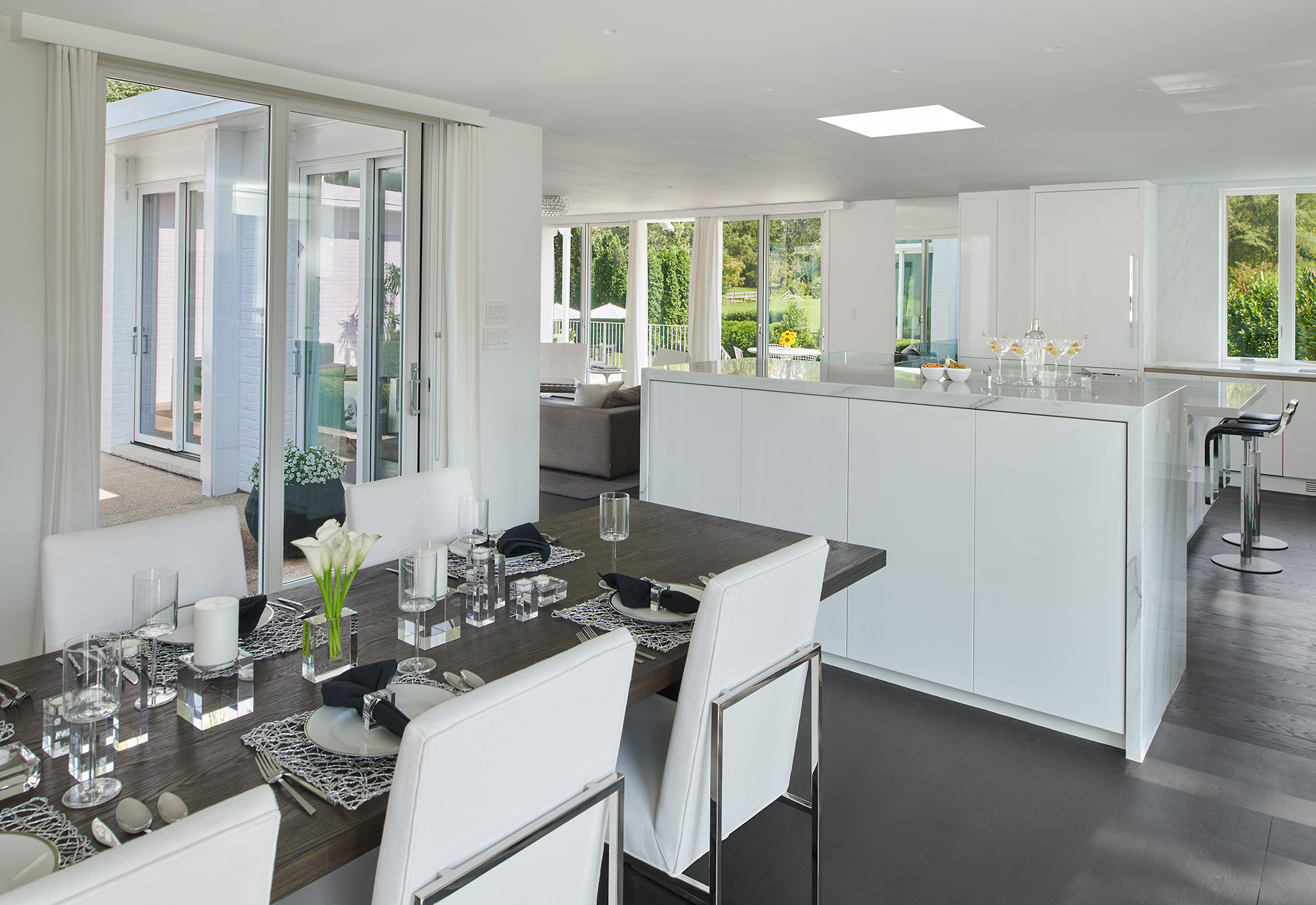Interior designed modern kitchen with dark hardwood dining table, white and silver dining chairs next to a high-top marbled granite bar table with built in storage